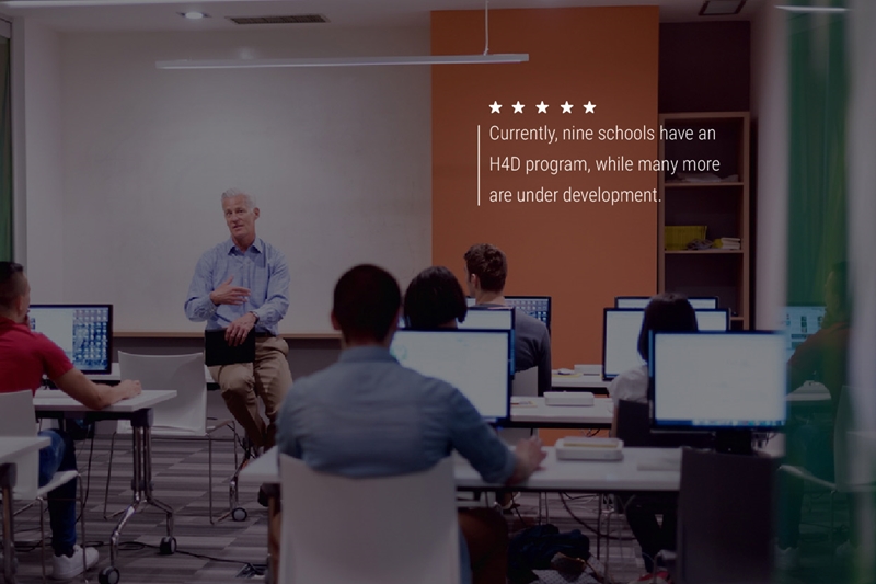 An older teacher sitting at the front of a college tech classroom. Text on the image reads "Currently, nine schools have an H4D program, while many more are under development."