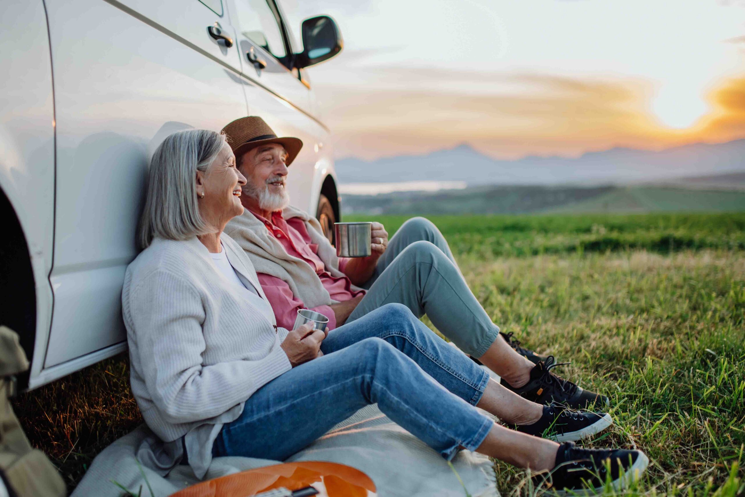 Senior couple sitting by car and drinking coffee after long drive during their roadtrip.